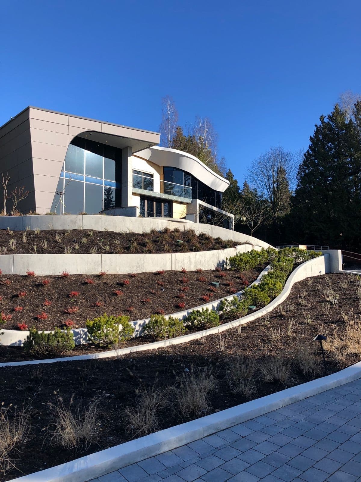 Modern home on a hillside with tiered board-formed concrete retaining walls and landscaping by MZ Solution